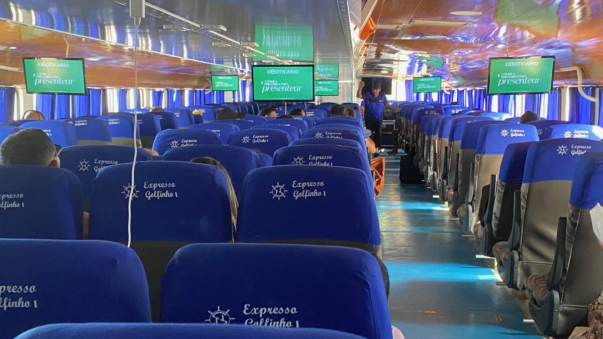 Telas exibindo campanha de O Boticário dentro da cabine da lancha Expresso Golfinho, com todos os assentos ocupados por passageiros