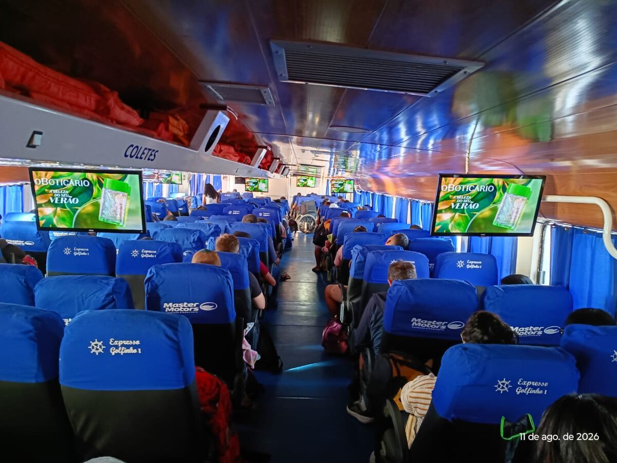 Cabine da lancha Expresso Golfinho com múltiplas telas exibindo simultaneamente a campanha Verão Amazônico de O Boticário, com todos os assentos ocupados por passageiros